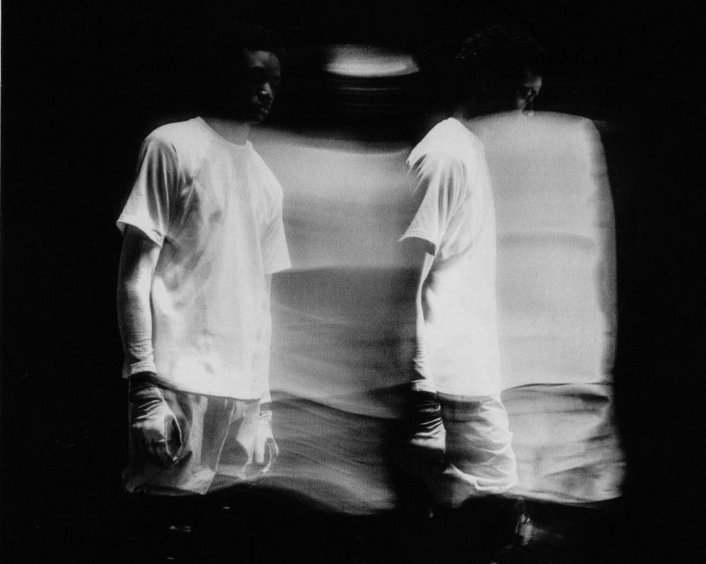 Black and white photo of a person wearing a white shirt and pants in a dark setting.